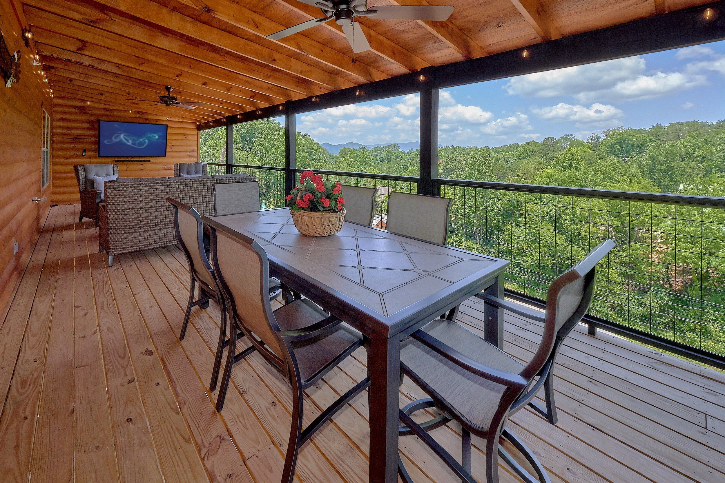 A wooden deck with a table and chairs, a ceiling fan, and a television.