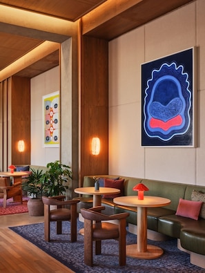 A modern lounge area with wooden flooring, green upholstered seating, and round tables. - 2 Queen Beds near Allston Square | Near MBTA Transit | Group Stay near Harvard (Boston)
