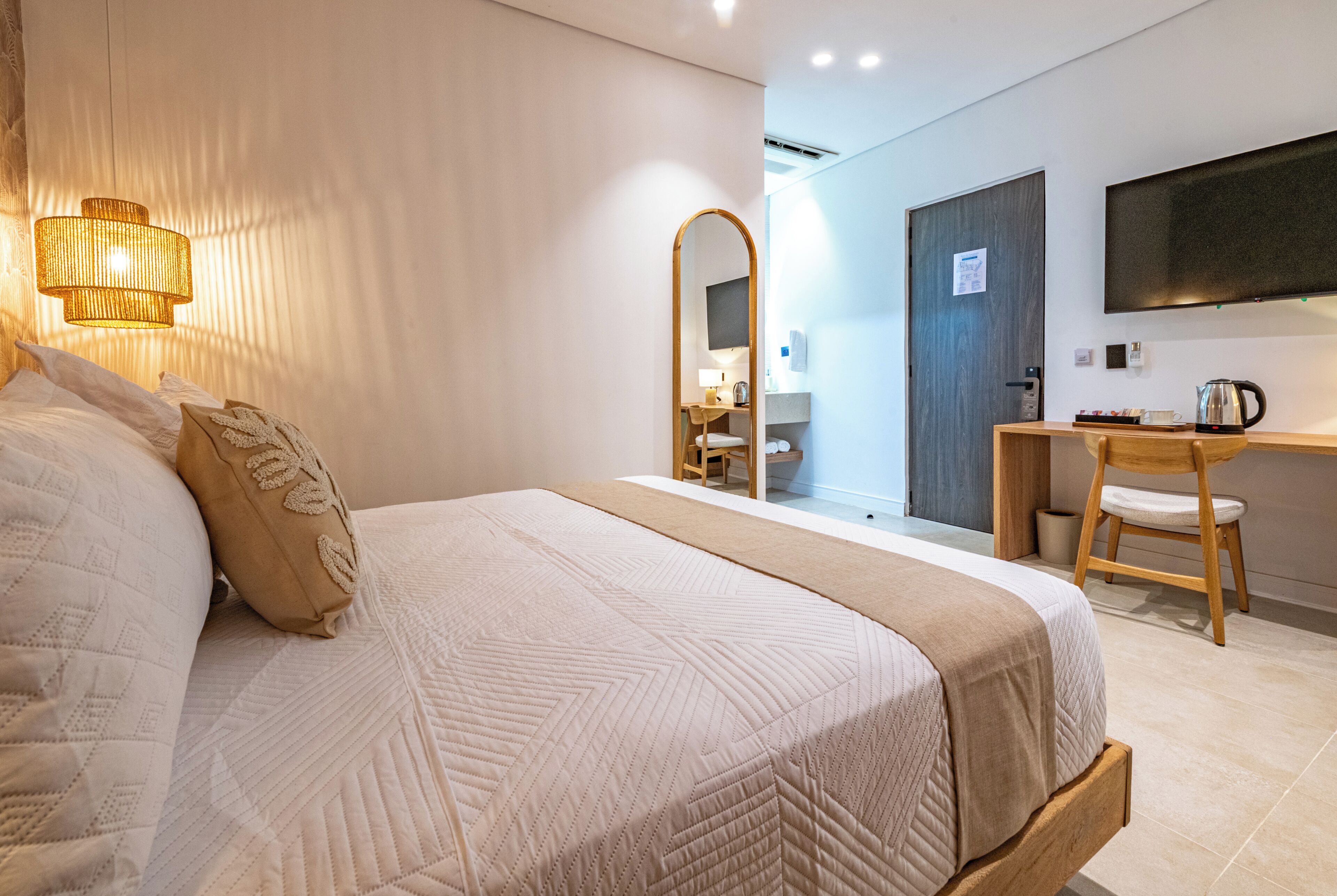 A hotel room with a large bed, a desk, a chair, a mirror, and a television on the wall.