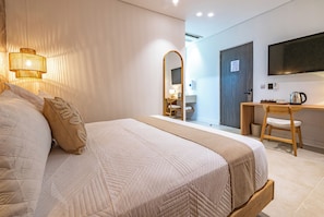 Habitación de hotel con una cama grande, un escritorio, una silla, un espejo y una televisión en la pared.