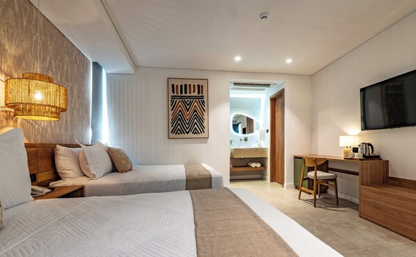 A hotel room with two beds, a desk, a chair, a television, and a bathroom visible through an open door.