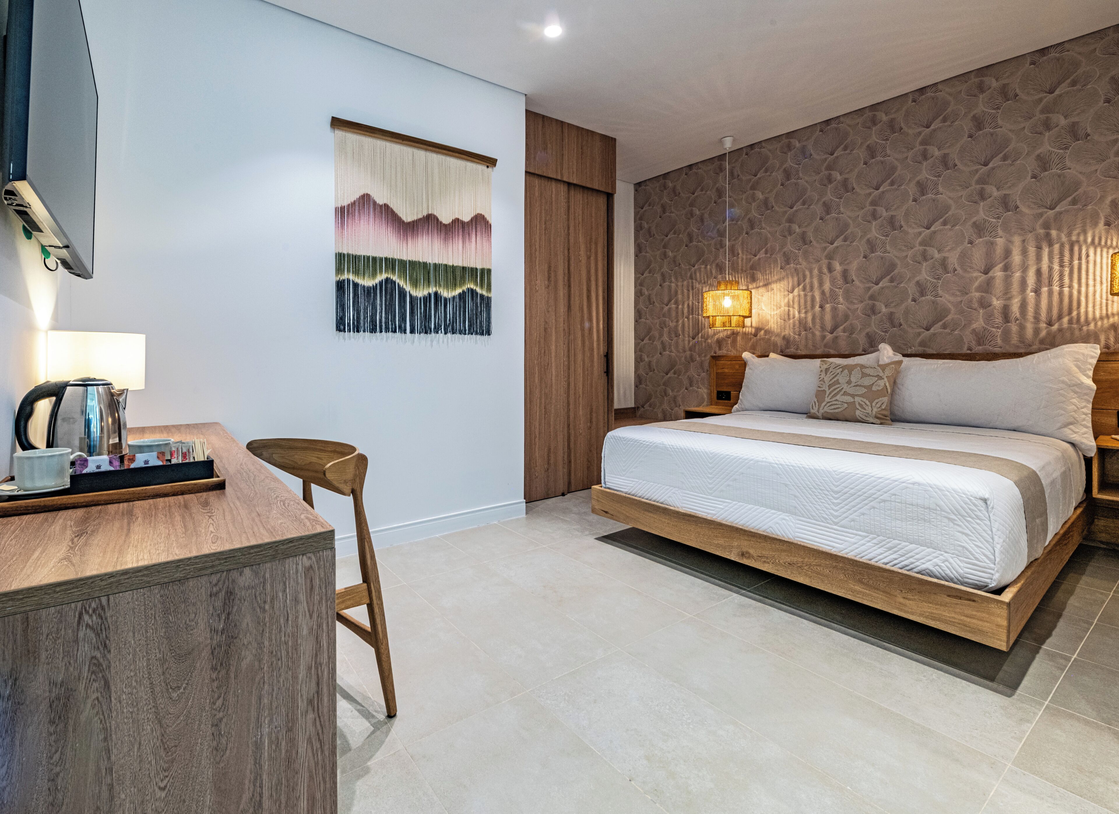 Una habitación de hotel moderna con un cabecero de madera, un escritorio con hervidor y una obra de arte colgada en la pared.