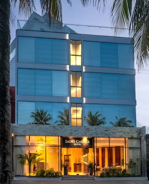 A modern hotel with a glass facade, a ground-level entrance with a sign, and a palm tree in the foreground. - Saint George Hotel (San Andrés)