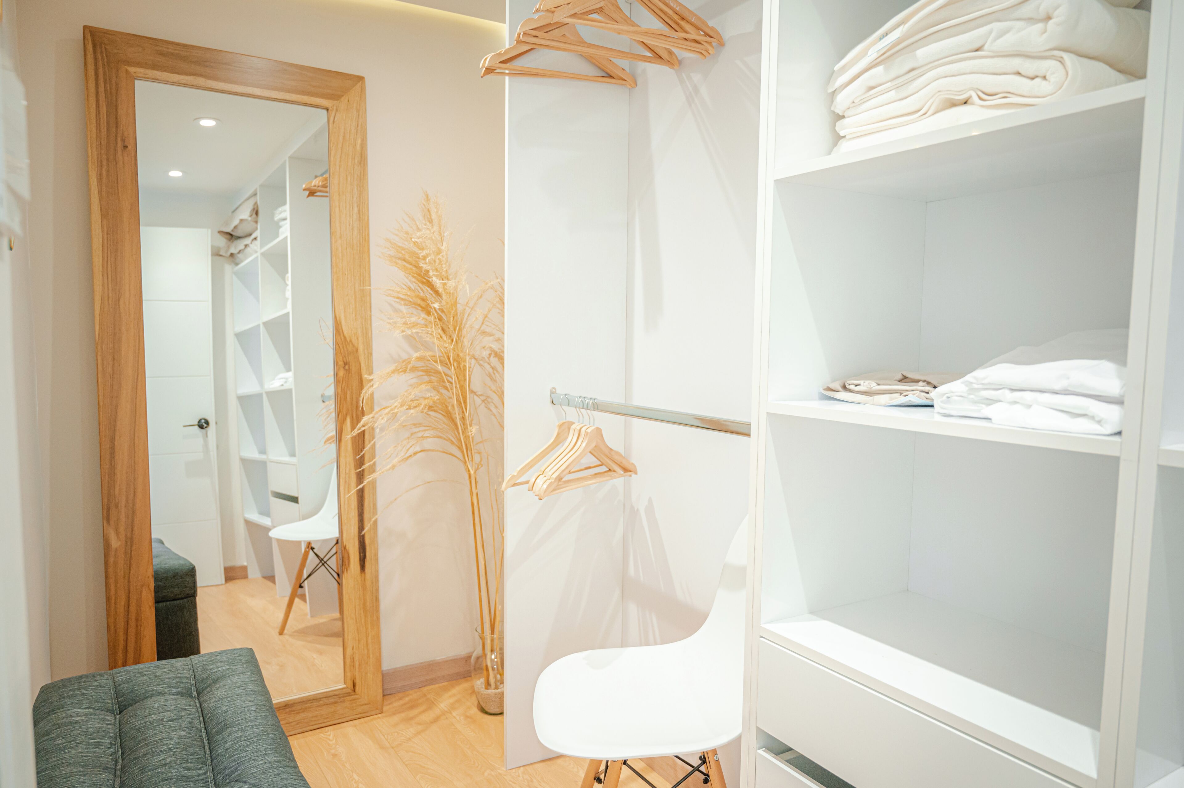 Ein modernes Hotelzimmer mit einer Holztür, einem weißen Stuhl, einer Glashaube und einem weißen Schrank mit gefalteten Handtüchern.