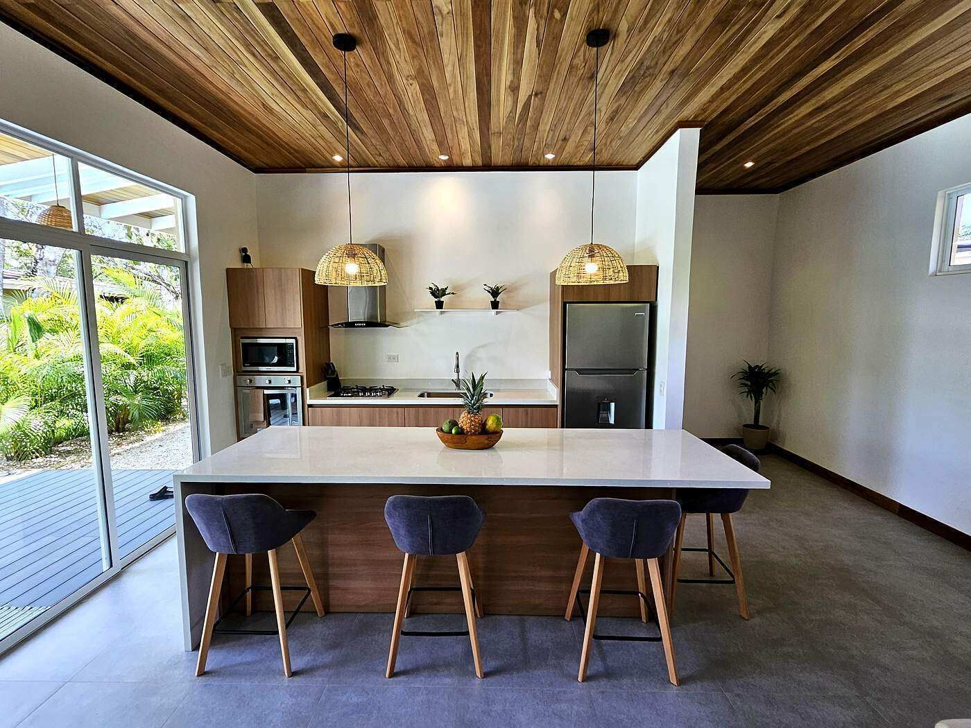 Une cuisine moderne dotée d’un grand îlot central, d’un plafond en bois et de tabourets de bar.