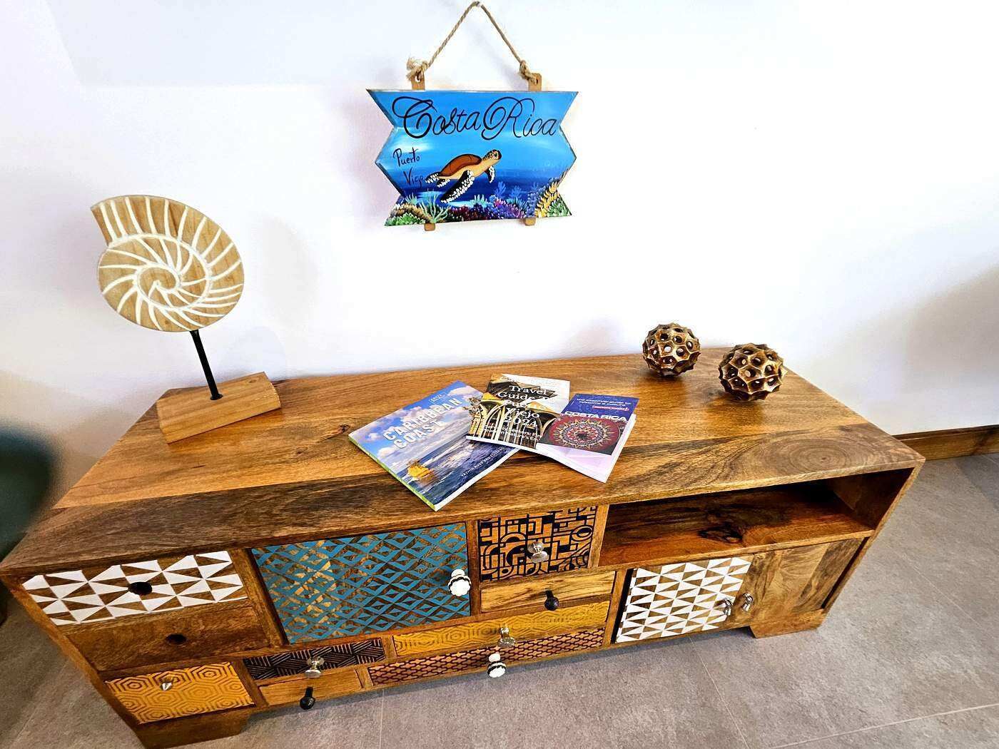 Una consola de madera con paneles decorativos, un cartel colgante y folletos de viajes.
