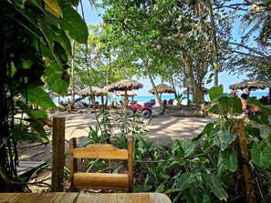 A beachside area with thatched umbrellas, a wooden bench, and a view of the sea. - Papi's Place: Private Pool Villa in Playa Negra, Costa Rica (Cahuita)