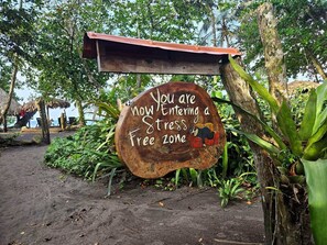 A wooden sign with a message about entering a stress-free zone, surrounded by tropical vegetation and a thatched structure. - Papi's Place: Private Pool Villa in Playa Negra, Costa Rica (Cahuita)