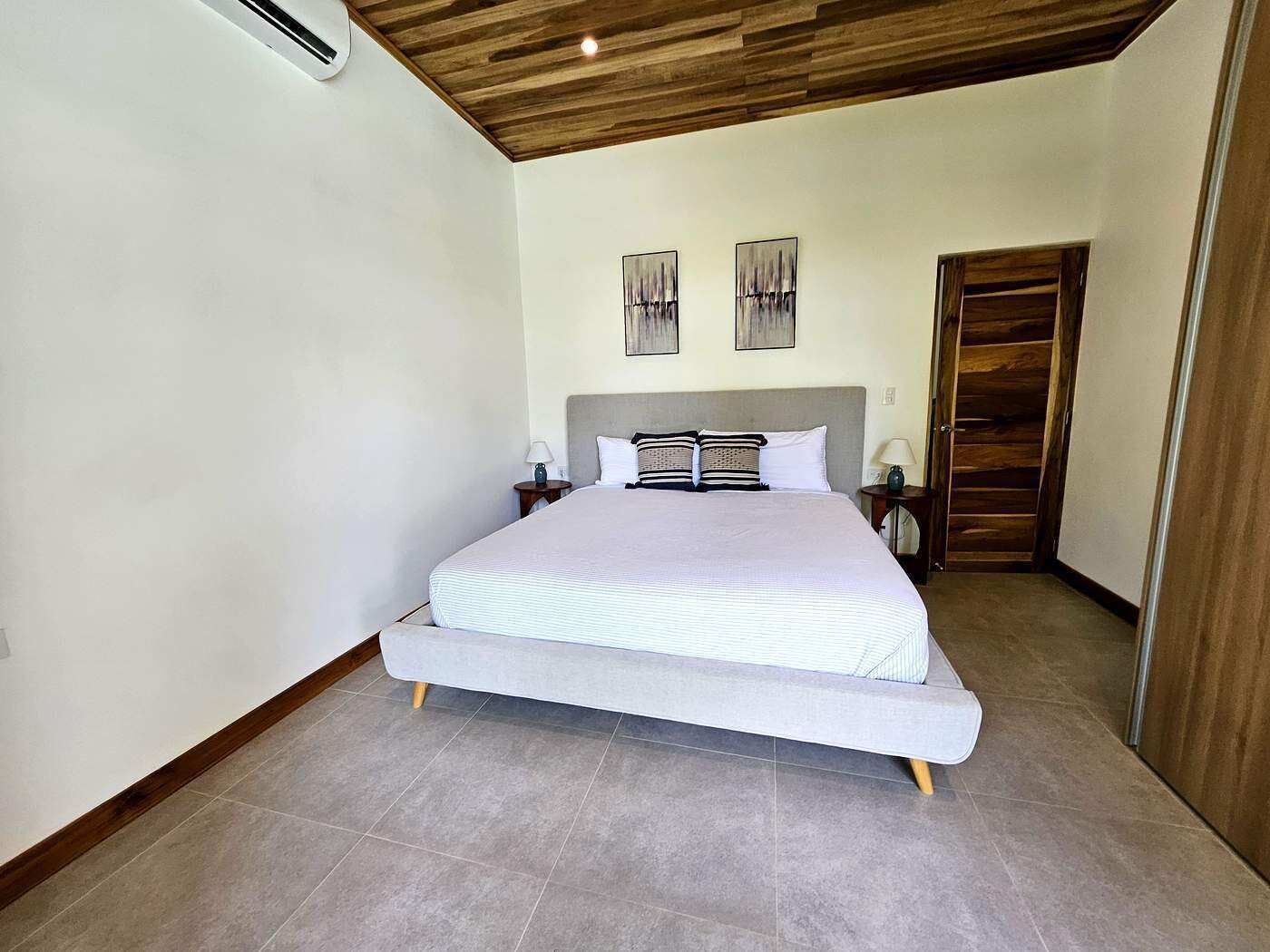 A bedroom with a bed, nightstands, a wooden ceiling, and a wardrobe.