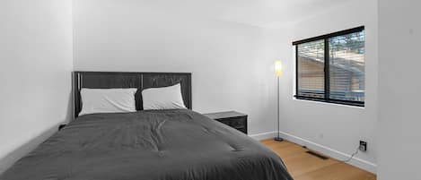 A bedroom with a bed, bedside table, lamp, and a window with blinds.