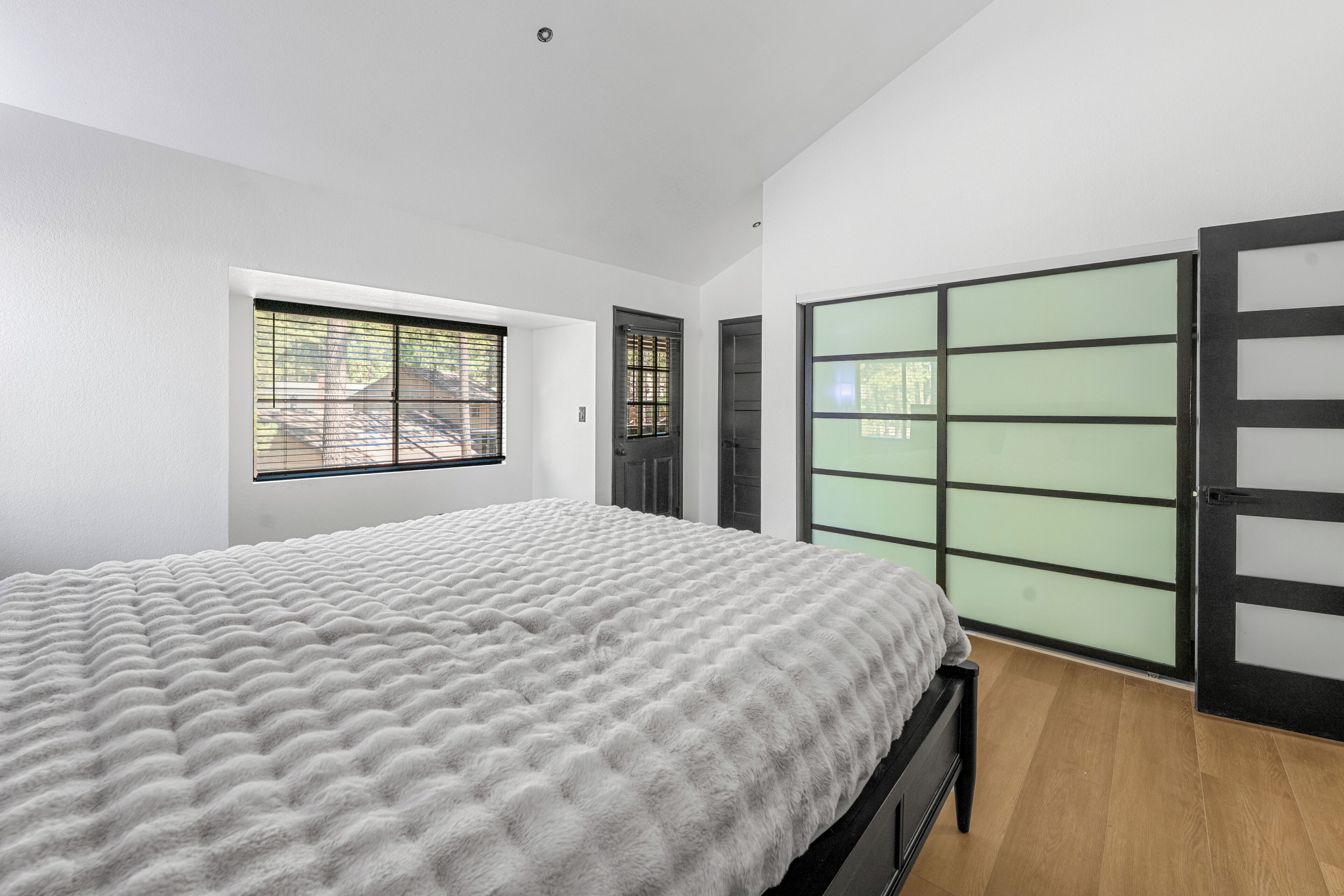A bedroom with a bed, a window, a door, and a sliding glass door.