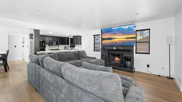 Una sala moderna con un amplio sofá seccional gris, una chimenea y un televisor de pantalla plana grande montado encima.
