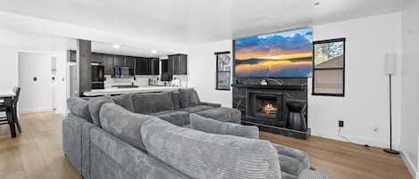 A modern living room with a large gray sectional sofa, a fireplace, and a large flat-screen TV mounted above it.