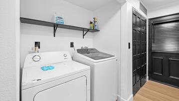 A laundry area with a front-loading washer and dryer, a shelf with cleaning supplies, and a black door.