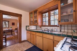 A kitchen with wooden cabinets, a microwave, a stove, and a window with stained glass.