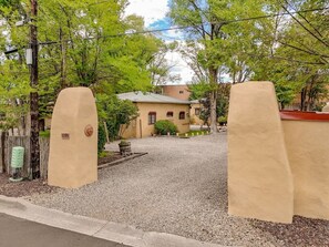 A gated entrance with a gravel driveway leading to a building with a tiled roof.