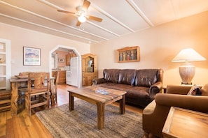 A cozy living room with a brown leather sofa, wooden coffee table, and a dining area with a wooden table and chairs.