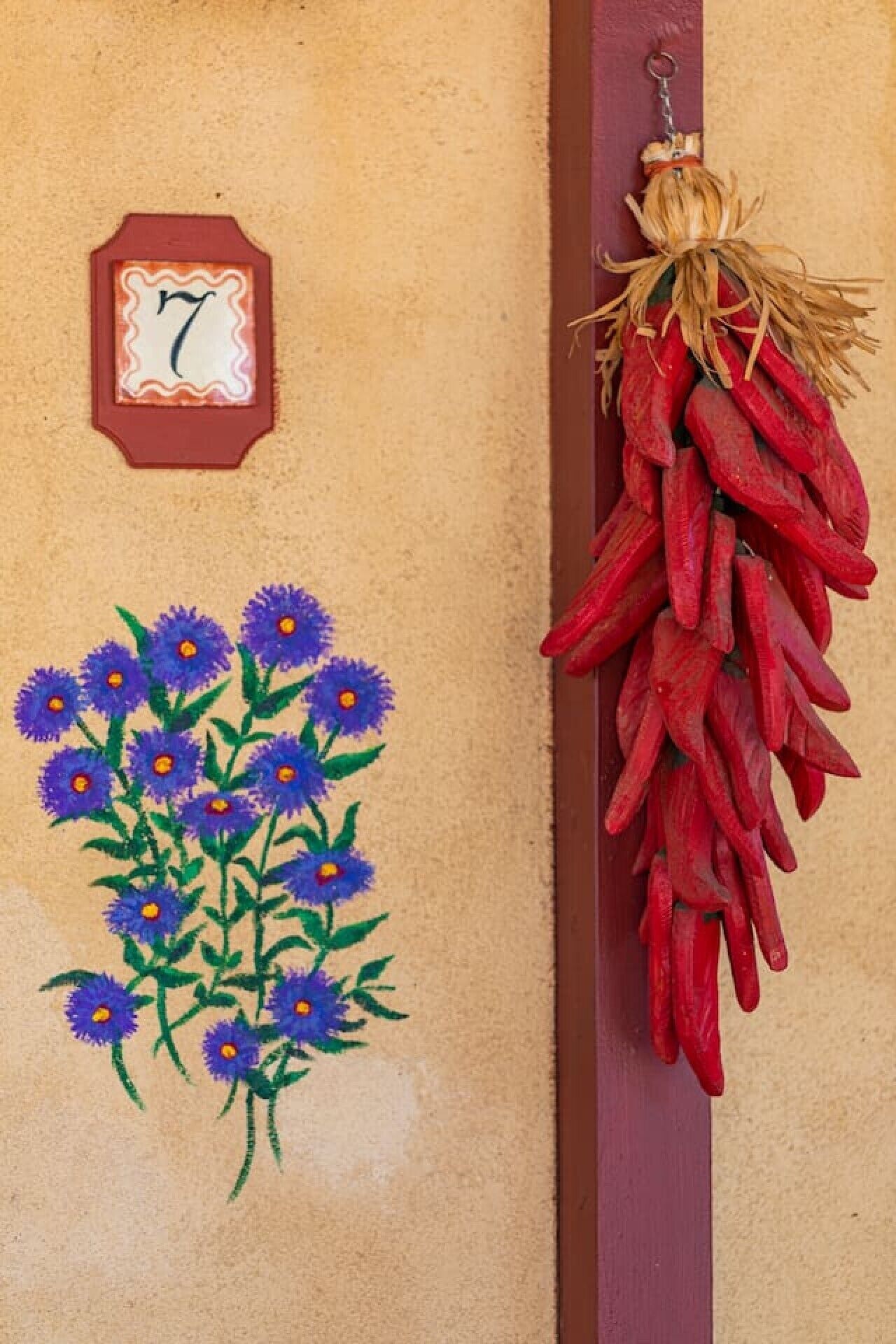 A wall with a number plaque, a painted flower arrangement, and a red chili pepper garland.