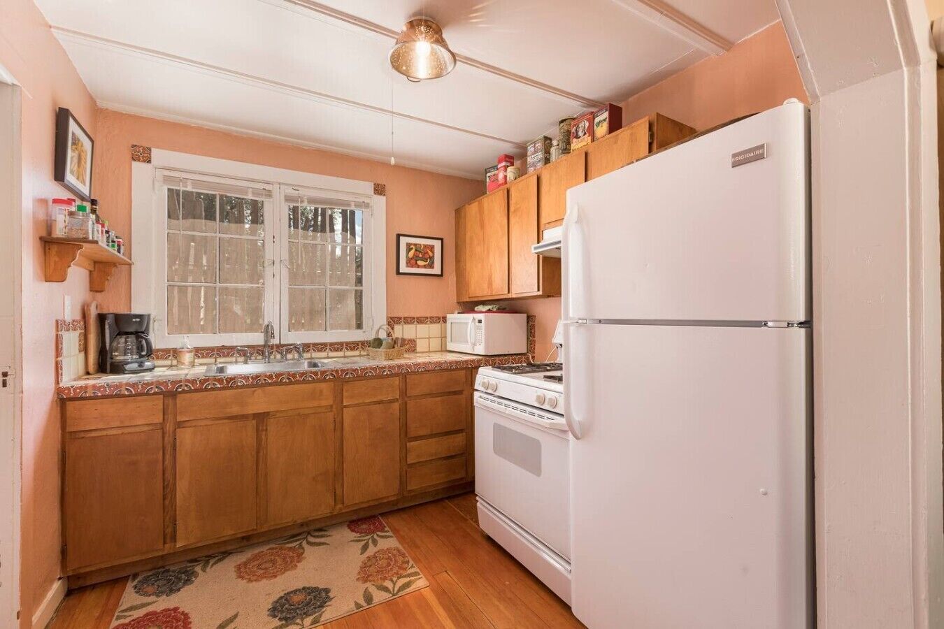 A kitchen with wooden cabinets, a white refrigerator, a stove, a microwave, and a window with a view.
