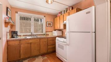 A kitchen with wooden cabinets, a white refrigerator, a stove, a microwave, and a window with a view.
