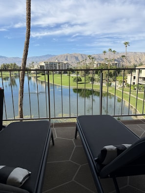 Un balcon doté de chaises longues, offrant une vue sur un lac, un terrain de golf et une chaîne de montagnes.