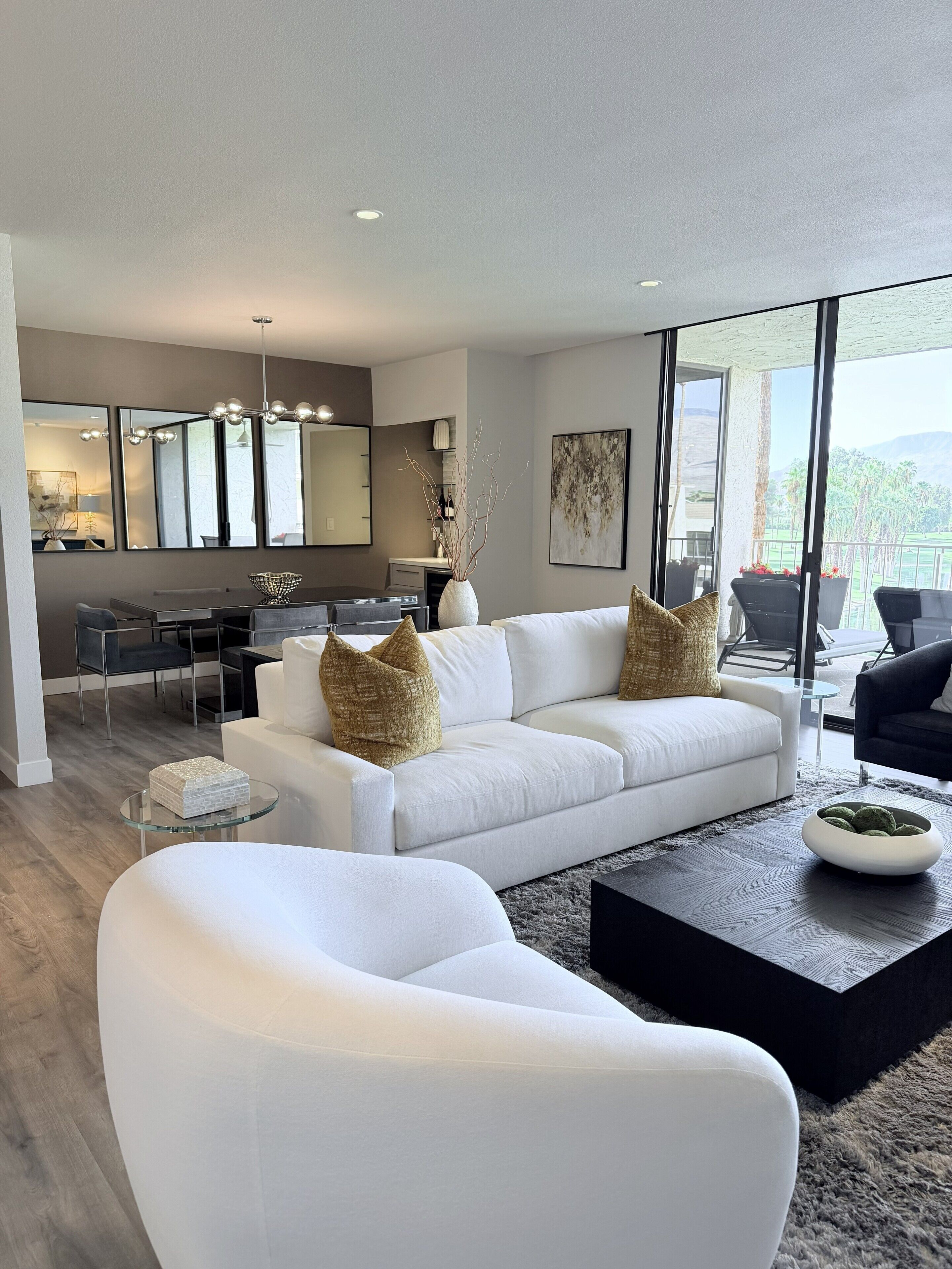 A modern living room with a white sofa, a glass coffee table, and a dining area with a white table and chairs.