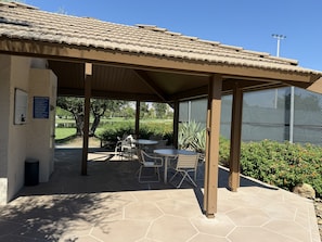 Ein überdachter Patio-Bereich mit Tisch und Stühlen, ein Schild für einen Tennisplatz und Blick auf einen Golfplatz.