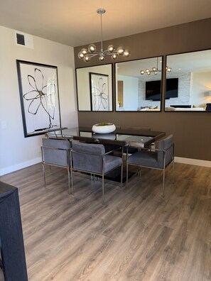 A modern dining area with a central table, four chairs, and a chandelier. - Spacious Contemporary -- Striking Mountain Views 2B/2BA in Coveted Desert Island (Rancho Mirage)