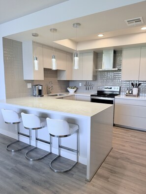A modern kitchen with a central island, bar stools, stainless steel appliances, and pendant lighting. - Spacious Contemporary -- Striking Mountain Views 2B/2BA in Coveted Desert Island (Rancho Mirage)