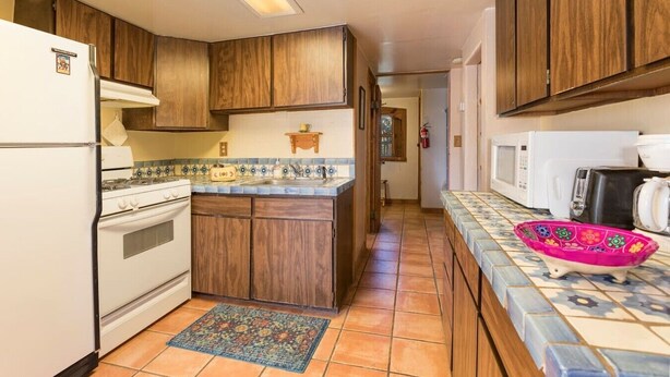 A kitchen with wooden cabinets, a tiled backsplash, a gas stove, a microwave, and a colorful bowl on the counter.