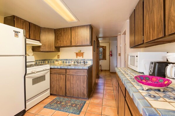 A kitchen with wooden cabinets, a tiled backsplash, a gas stove, a microwave, and a colorful bowl on the counter.