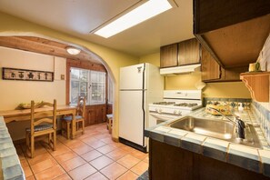 Cocina compacta con comedor, armarios de madera, refrigerador y salpicadero de azulejos.