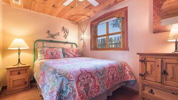 A bedroom with a bed, a nightstand, a dresser, a window, and a ceiling fan.