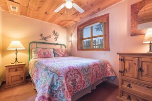 Un dormitorio con cama, mesita de noche, cómoda, ventana y ventilador de techo.