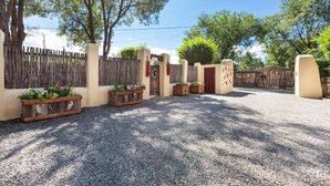 A gravel driveway leading to a gated entrance with wooden planters and a red door.