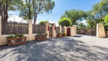 A gravel driveway leading to a gated entrance with wooden planters and a red door.