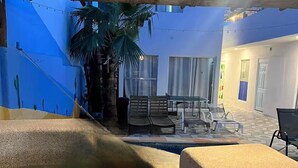 Ein Poolbereich mit Palme, Gartenmöbeln und einer hängenden Leuchte.