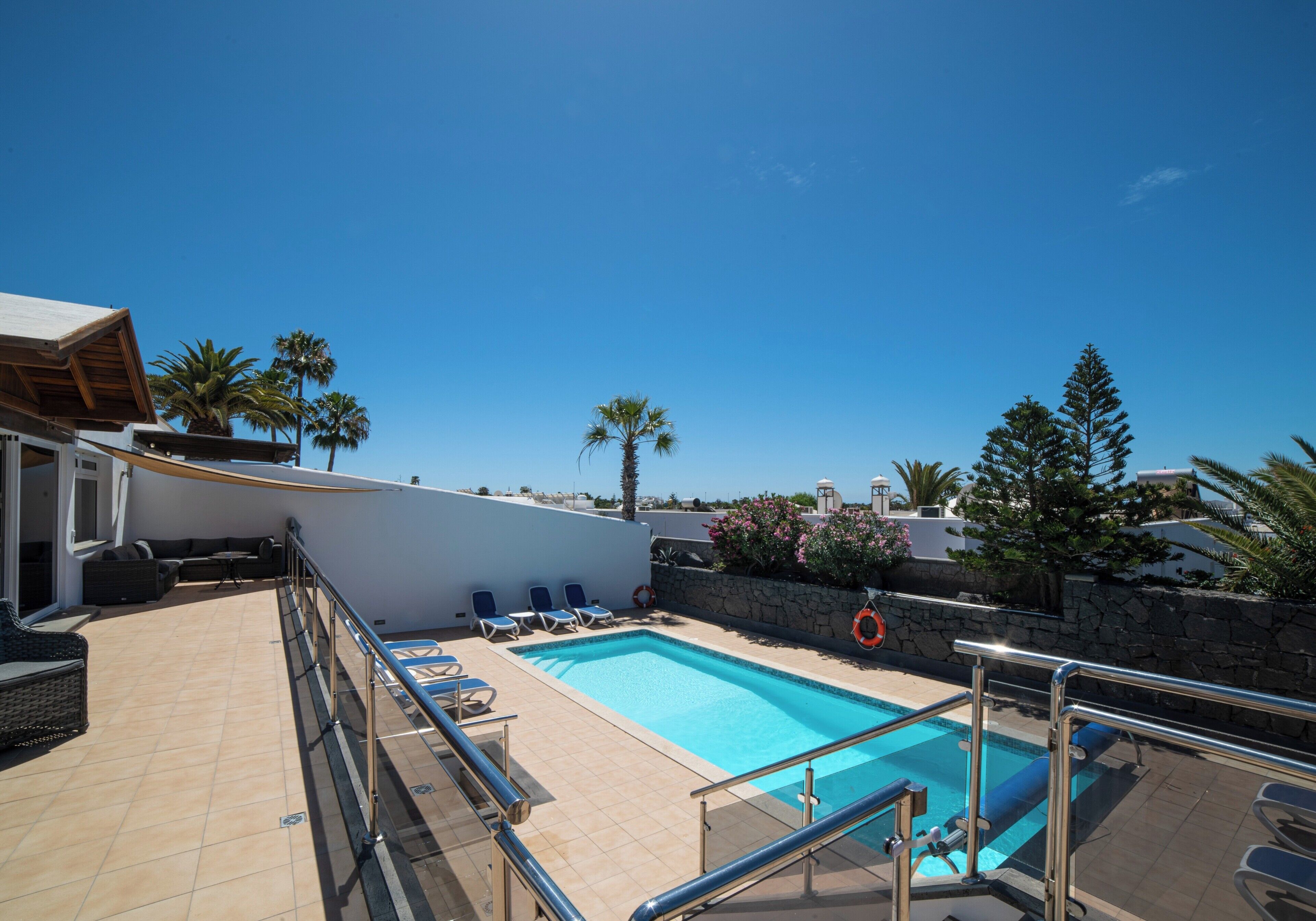 Un área de piscina con cielo azul despejado, piscina, sillas de descanso y una pared de piedra.