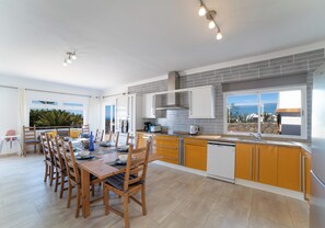 A modern kitchen with a dining area, featuring a large window with a view, a built-in oven, and a dishwasher. - Large 4 Bedroom Villa Featuring Hot Tub, Private Pool & Air Con (Playa Blanca)