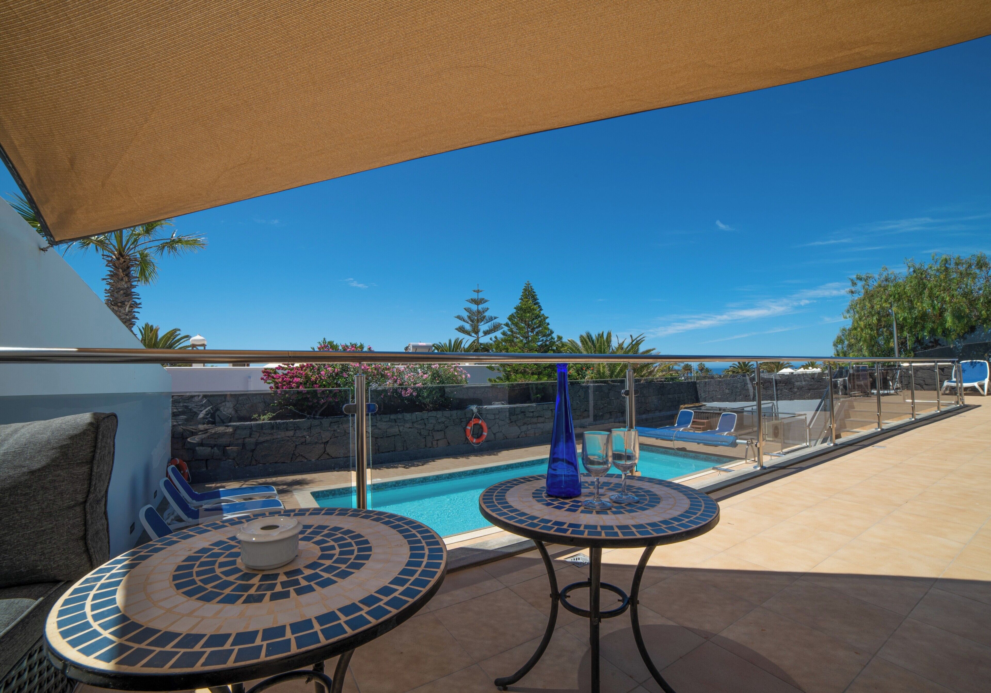 Zona de piscina con dos mesas de cerámica, una silla de descanso y vistas a la piscina y el paisaje circundante.