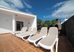 Eine Dachterrasse mit Liegestühlen, einer Steinmauer und einem modernen Gebäude mit Schornstein.