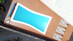 An aerial view of a rectangular swimming pool with a tiled border, surrounded by a brick patio. - Relaxing & Private 3 Bedroom & 3 Bathroom Villa (Playa Blanca)