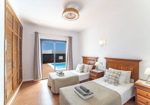 A hotel room with two beds, a wooden headboard, a nightstand, a lamp, and a view of a swimming pool. - Relaxing & Private 3 Bedroom & 3 Bathroom Villa (Playa Blanca)