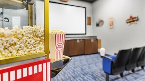 A snack bar with popcorn and a drink dispenser, a projection screen, and seating area with chairs.