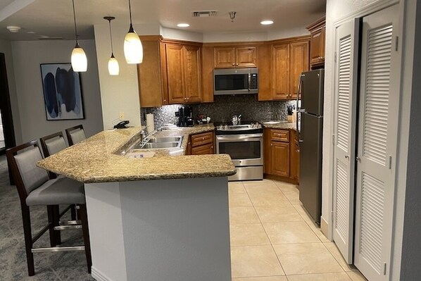 A modern kitchen with granite countertops, wooden cabinets, stainless steel appliances, and pendant lighting.