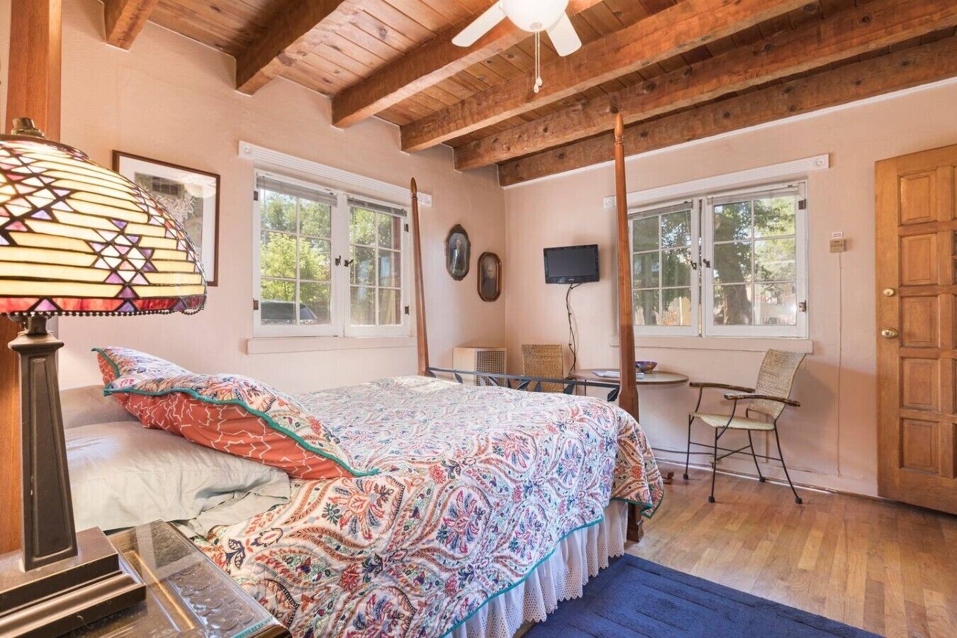 A bedroom with a bed, a desk, and a chair. There are windows and a door.