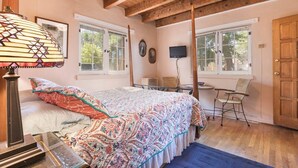 A bedroom with a bed, a desk, and a chair. There are windows and a door.