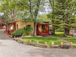 A traditional wooden house with a porch, surrounded by trees and a gravel driveway.