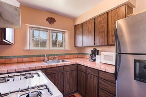 A kitchen with a gas stove, stainless steel refrigerator, wooden cabinets, a window with blinds, and a tiled backsplash.