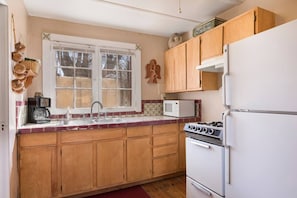A kitchen with wooden cabinets, a white refrigerator, a stove, a microwave, and a window with a view of trees.